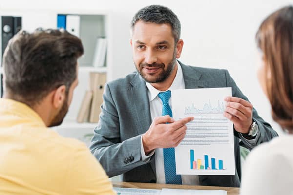 At Virtus Wealth Management and Financial Advisers, specialize in investment advice for people looking for healthy returns and low risk investments. Image of a financial advisor showing a couple a financial document with tables and graphs.