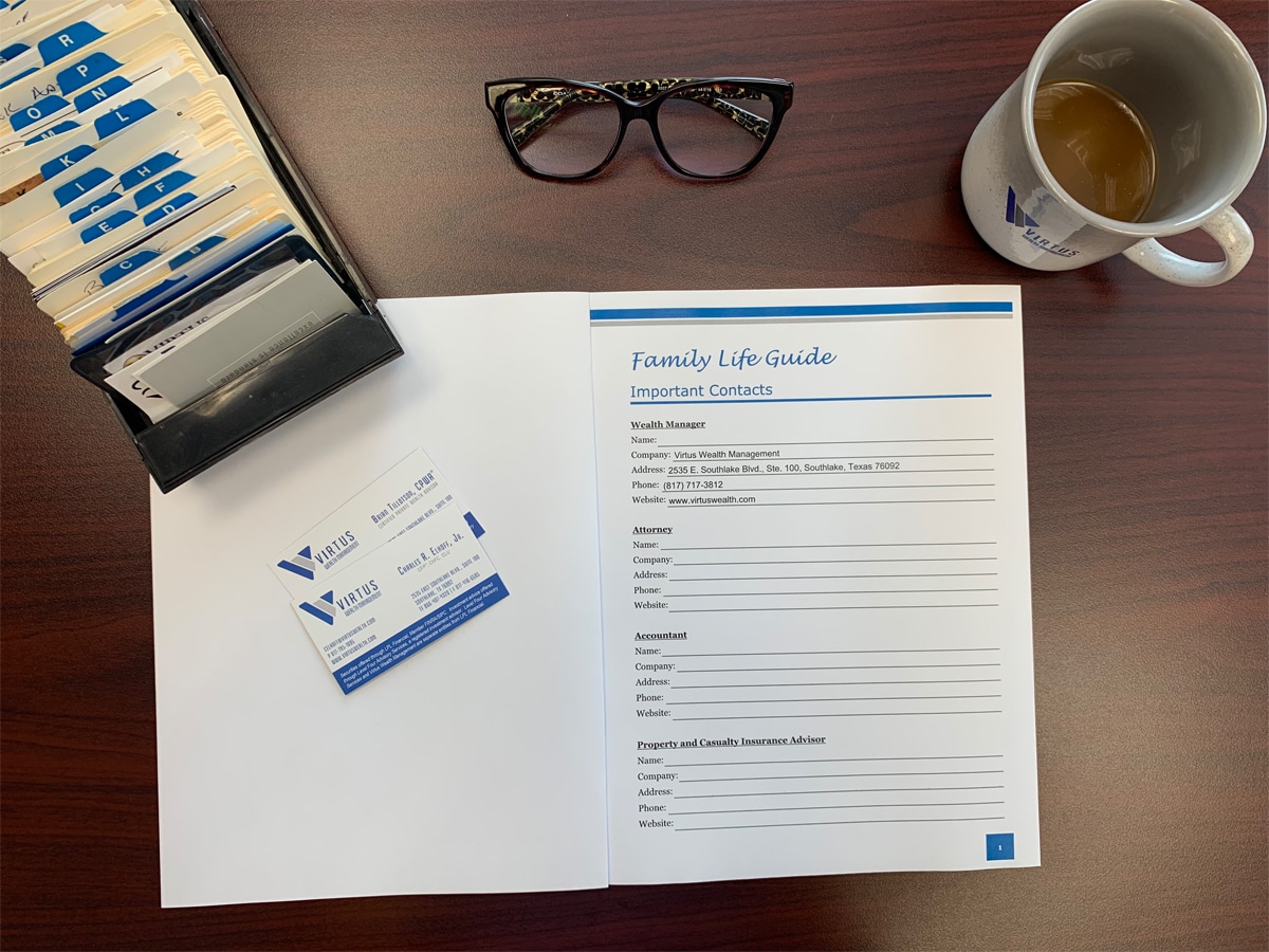 A rolodex, glasses, and a cup of coffee all sit on top of a wooden desk surrounding an open book that reads "Family Life Guide"