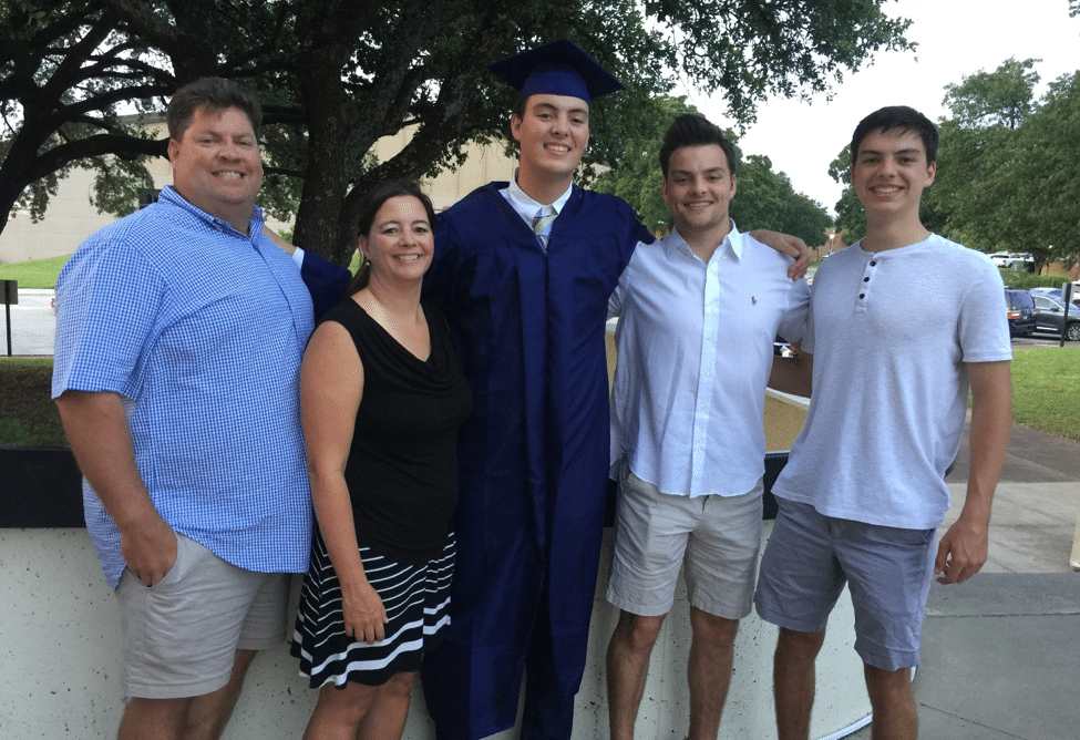 Graduate in cap and gown standing with family outdoors