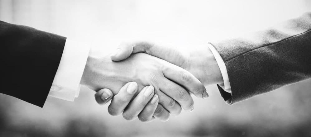 A close-up black and white photo of two people wearing suits shaking hands.