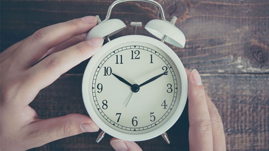 Hands surrounding a white alarm clock
