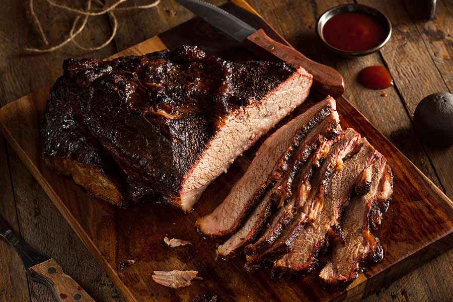 Sliced smoked barbecue on a cutting board with sauce