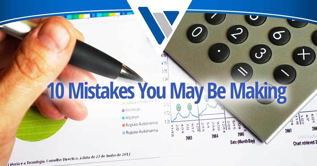 Hand holding a pen beside a calculator and financial charts